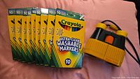 Nine packs of Crayola Ultra-Clean Washable Markers next to a pair of yellow and gray Fisher-Price binoculars on a pink surface.