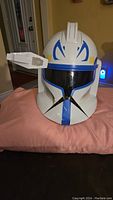 Front view of the white Star Wars Captain Rex helmet with blue markings and black visor on pink pillow.
