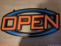 Front view of LED open sign showing orange 'OPEN' letters on blue and black background.
