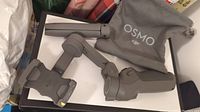 DJI Osmo handheld gimbal stabilizer partially folded, displayed on a box with grey pouch beside it.