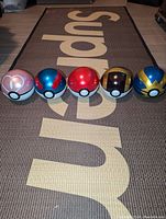 Five empty Pokeballs arranged in a row on a rug with a Supreme logo visible beneath.