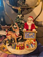 Front view of the full ceramic figurine including Santa, reindeer, elf, gifts, Christmas tree, and sleigh toys.
