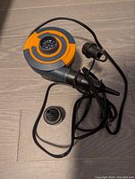 Sidewinder electric air pump with orange and black casing, power cord, and two inflation nozzles shown on wooden floor