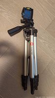 Folded Simmons tripod showing silver legs, black plastic components, and mounting head with handle.