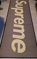 Top view of the bamboo mat unrolled with the word 'Supreme' displayed in large beige letters on a dark brown background.
