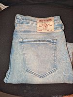 Folded light blue denim jeans showing back pocket and True Religion brand patch on waistband.