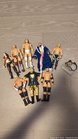 Lot of 9 WWE wrestling action figures and 1 belt accessory arranged on floor showing overall condition and variety.