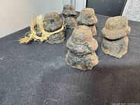 Five antique cast iron Burmese style opium weights arranged on a black surface, showing irregular diverse shapes and one tied with a natural fiber string.