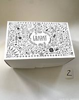 Closed white cardboard box lid with black detailed nature and craft-themed illustrations and the text 'GRAPAT' in the center