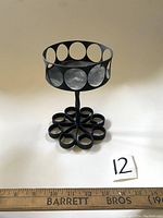 Full view of the black iron candle holder showing circular cut-out pattern on upper rim and flower-shaped base with rounded loops. Wooden ruler in front for size reference measuring approximately 7 inches tall.
