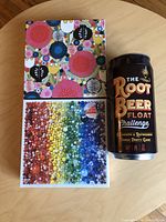 Lot showing two Gallison 500-piece puzzles and the Root Beer Float Challenge game in a sealed can.