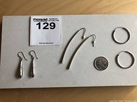 All three pairs of silver earrings displayed with a quarter for scale: stamped Birks sterling drop earrings, minimalist curved bar earrings, and simple silver hoops.