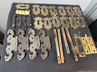 Top-down view showing all items in the lot including door handles, keyhole plates, hinges, and mounting plates placed on black fabric