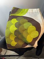 Folded vintage curtain panel showing large circle pattern with green and yellow hues on beige background.