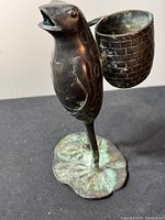 Front angle of bronze frog statue showing standing frog with open mouth and basket on back, placed on textured lily pad base.