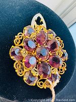 Front view showing purple faceted glass stones set in gold-tone filigree forming a floral pattern.