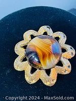 Brooch showing textured gold-tone metal flower shape with round brown wavy glass center, angled view