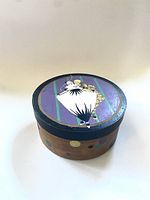 Top view of the round wooden box showing the hand-painted vintage art featuring three figures on a purple and green striped background, surrounded by multicolored polka dots on the edge of the lid.