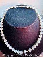 Full view of the vintage knotted opalescent glass beaded necklace displayed on black jewelry stand, showing circular translucent baby blue beads with an iridescent finish.