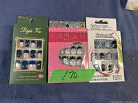 Three packs of fake nails in various designs and colors on a blue surface.