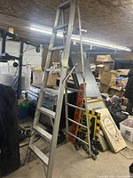 Full view of the 8-foot aluminum step ladder standing upright in a cluttered basement or storage area showing its overall structure and condition.