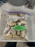 Plastic bag containing multiple used natural cork wine stoppers with various logos and designs visible through the bag.