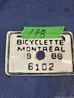 Photo of a rectangular white metal Montreal bicycle license plate from 1986 with black embossed text and registration number 6102.
