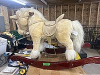 Side view of the child's rocking horse showing plush beige horse mounted on a dark red curved wooden rocker base with decorative scrollwork.