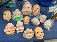 Photo showing twelve vintage doll faces with various facial features and expressions arranged on a blue fabric background.