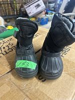 Front view of pair of black winter boots, showing rubber soles and quilted upper with strap at top.