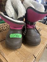 Front view of the pair of girls' winter boots showing the pink upper and brown rubber sole with a green sticker indicating size/price.