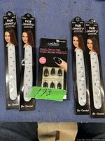 Two packs of silver hair jewelry and one pack of black metallic fake nails on a dark surface.