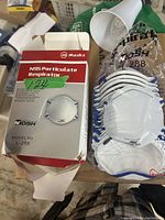 Open box showing multiple white N95 masks with blue edging and the box itself marked with NOSH brand and model L-288.