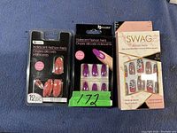 Photo of three unopened packs of fake nails: two from Choice brand labeled 'Iridescent Fashion Nails' in orange and purple shades, and one from Swag Collection with mixed pattern designs.