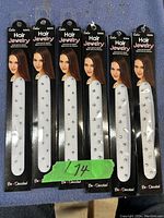 Photo showing six identical white hair clips decorated with small rhinestones, attached to black cards branded 'Cala Hair Jewelry' with a female model image.