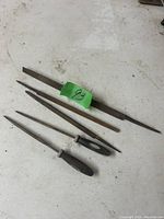 Five metal files laid out on a white surface, showing variety of sizes and types, two with black plastic handles.