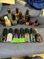 Photo showing 14 used nail polish bottles on a blue surface in various colors and brands.