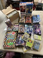 Photo showing various loose Pokemon cards, booster packs, boxed puzzles, and a Pokemon handbook displayed on a table.