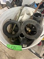 Top view of white pail filled with various plumbing parts, including rubber gaskets, PVC pipe fittings, brass fittings, and metal connectors