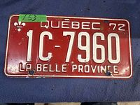 Photo of a single 1972 Quebec license plate showing red background with white embossed text and fleur-de-lis symbol. The plate reads 'QUÉBEC 72', '1C-7960', and 'LA BELLE PROVINCE'. Plate shows signs of age including minor rust and paint wear.