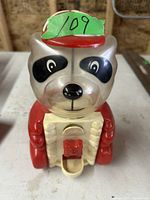 Front view of vintage bear gumball machine showing facial features, red arms, and dispensing chute with handle.