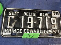 Front view of vintage Prince Edward Island license plate from 1979 showing embossed white lettering and black background, with 'SEAT BELTS SAVE' slogan and some wear marks.
