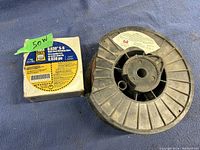 Photo showing spool of copper coated welding wire next to a box of Lincoln Electric Hobart S-6 welding wire.