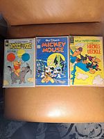 Three vintage comic books laid out side by side on a leather surface. Covers are colorful featuring Winnie the Pooh, Mickey Mouse, and New Terrytoons Heckle & Jeckle characters.