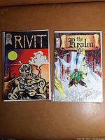 Photo showing two comic books titled 'Rivit' and 'The Realm' side by side on a brown surface.