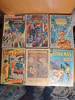 Photo showing six vintage comic books arranged in two rows on a wooden surface, covers visible with varying colors and themes.