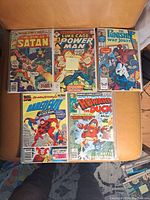 Top-down photo of five Marvel comic books placed on a tan leather surface. Comics include The Son of Satan, Luke Cage Power Man, The Punisher War Journal, Daredevil, and Howard the Duck.