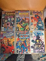 Photo showing six Marvel comic books including What If Punisher, What If Wolverine, The Punisher War Journal, The Spectacular Spider-Man, Marvel Tales Spider-Man Power Man, and Classic X-Men, arranged in two rows on a brown chair.
