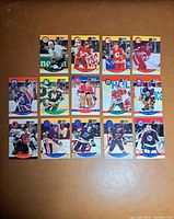 Front view of 15 hockey cards laid out on a brown surface showing various NHL players in action with colorful borders mainly red, yellow and blue.