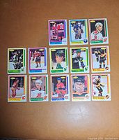 Front side of 14 vintage hockey cards arranged on surface showing player photos and team logos.